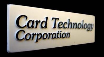 This metal nameplate is rectangular and features a clean white background. Across the center, bold black raised lettering displays the company name: "Card Technology Corporation." The high-contrast design ensures clarity and immediate brand recognition. The text stands out crisply against the white plate, while a subtle black background behind each letter enhances legibility and gives the logo an embossed look. This classic style is typical for professional corporate signage, drawing attention to *Card Technology Corporation* in a sleek, modern fashion.