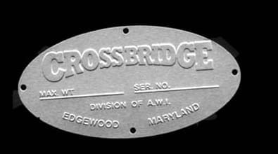 The metal nameplate is oval-shaped, featuring the company name “CROSSBRIDGE” prominently across its center. Beneath this title, there are designated spaces labeled “MAX. WT” and “SER. NO.” for recording maximum weight and serial number information. Below these sections, the plate is inscribed with “DIVISION OF A.W.A.,” followed by location details: “EDGEWOOD” and “MARYLAND.” Each edge of the nameplate has a single hole—four in total—presumably for mounting onto equipment or machinery. The layout and markings suggest it serves as an identification or specification tag for products made by Crossbridge, a division of A.W.A., based in Edgewood, Maryland.