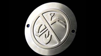 A round metal nameplate sign with a crossed-out symbol of a hard hat, shovel, and person digging, clearly indicating that no digging is allowed.