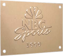 This is a metal nameplate prominently displaying the NBC Sports corporate identity. At the center, it features the well-known NBC logo: a colorful, stylized peacock emblem, immediately recognizable as a symbol of NBC. Beneath or beside the peacock is the "NBC Sports" wording, rendered in distinctive, stylized text that conveys both professionalism and brand personality. Below this branding, "1999" is neatly engraved to indicate either the year of production or significance. The rectangular plate has four holes—one in each corner—designed for easy mounting onto surfaces such as walls or equipment. Crafted from durable metal and marked with both company name and iconic logo, this nameplate serves as an official display piece commemorating NBC Sports in 1999.