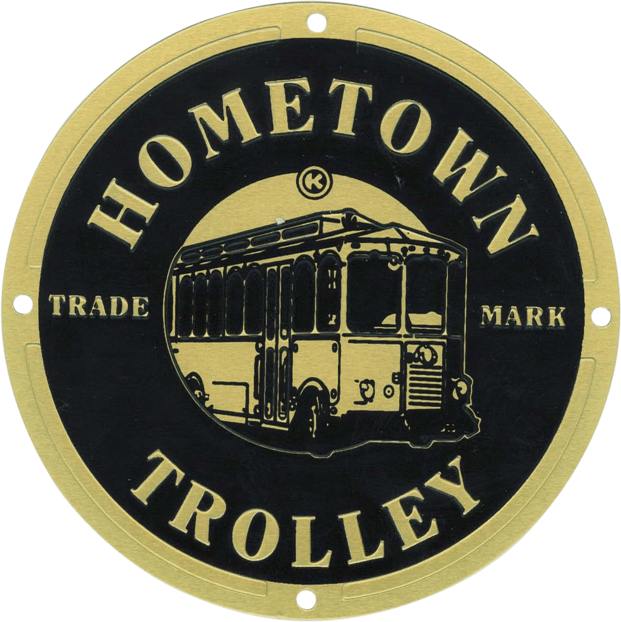 This metal nameplate is a round, emblem-style badge crafted in gold and black tones. At its center, it features a detailed illustration of a vintage trolley car, emphasizing the brand’s nostalgic charm and historic roots. Encircling the trolley illustration are the words "Hometown Trolley" prominently displayed around the outer edge of the nameplate, highlighting the company’s identity. Flanking either side of the central trolley image are small inscriptions reading "Trade Mark," signifying authenticity and registered branding. The overall design combines classic elegance with industrial durability, making it an instantly recognizable emblem for Hometown Trolley products.
