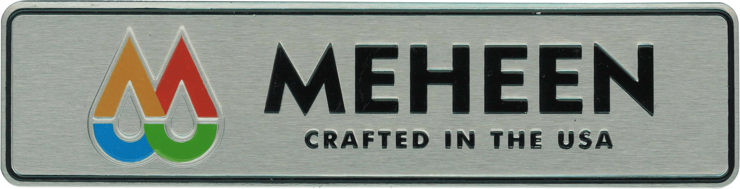 This metal nameplate features a distinctive multicolored "M" logo on the left, representing the Meheen company. To the right of the logo, bold black lettering spells out "MEHEEN CRAFTED IN THE USA," clearly highlighting both the brand and its American manufacturing origin. The combination of striking colors in the "M" and strong typography gives the nameplate a professional and eye-catching appearance, typical for industrial or commercial equipment branding.