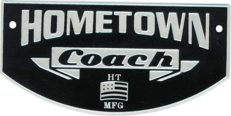 This metal nameplate features the company name "HOMETOWN Coach" boldly etched across the top. Beneath, there's a prominent logo combining the letters “HT” and “MFG”, divided by a stylized, abstract American flag motif, symbolizing pride in domestic manufacturing. The plate is designed with two pre-drilled holes on each side for easy mounting. Its overall aesthetic conveys strength and craftsmanship—ideal for branding vehicles or equipment produced by Hometown Coach Manufacturing.